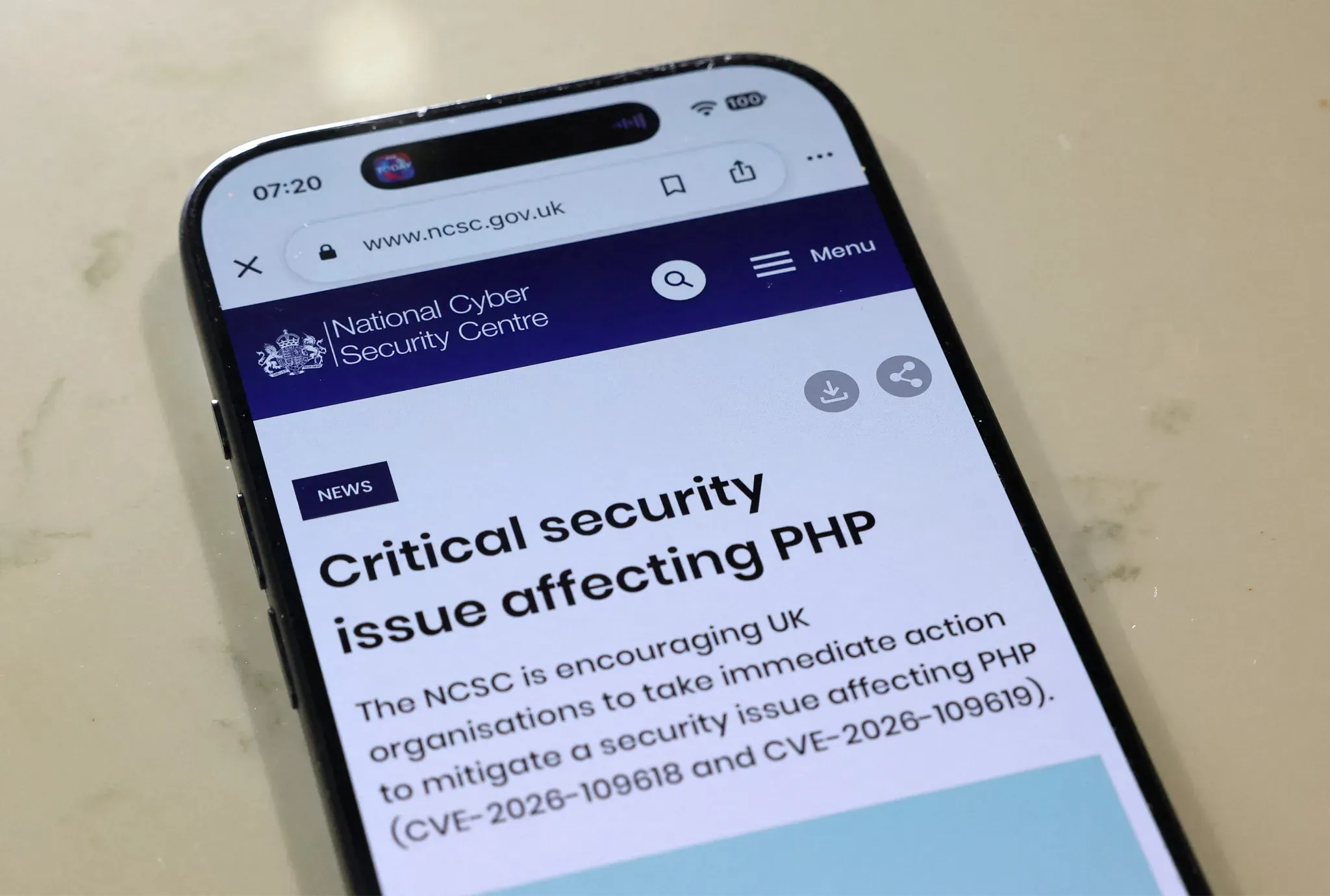 A phone showing the UK National Cyber Security Centre news page "Critical security issue affecting PHP", urging organisations to act on CVE-2026-109618 and CVE-2026-109619